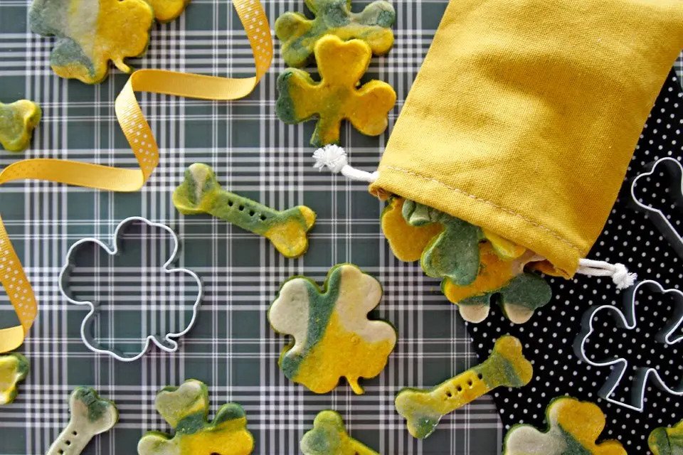 Colorful green and yellow dog treats splayed out on a table with shamrock shaped cookie cutters